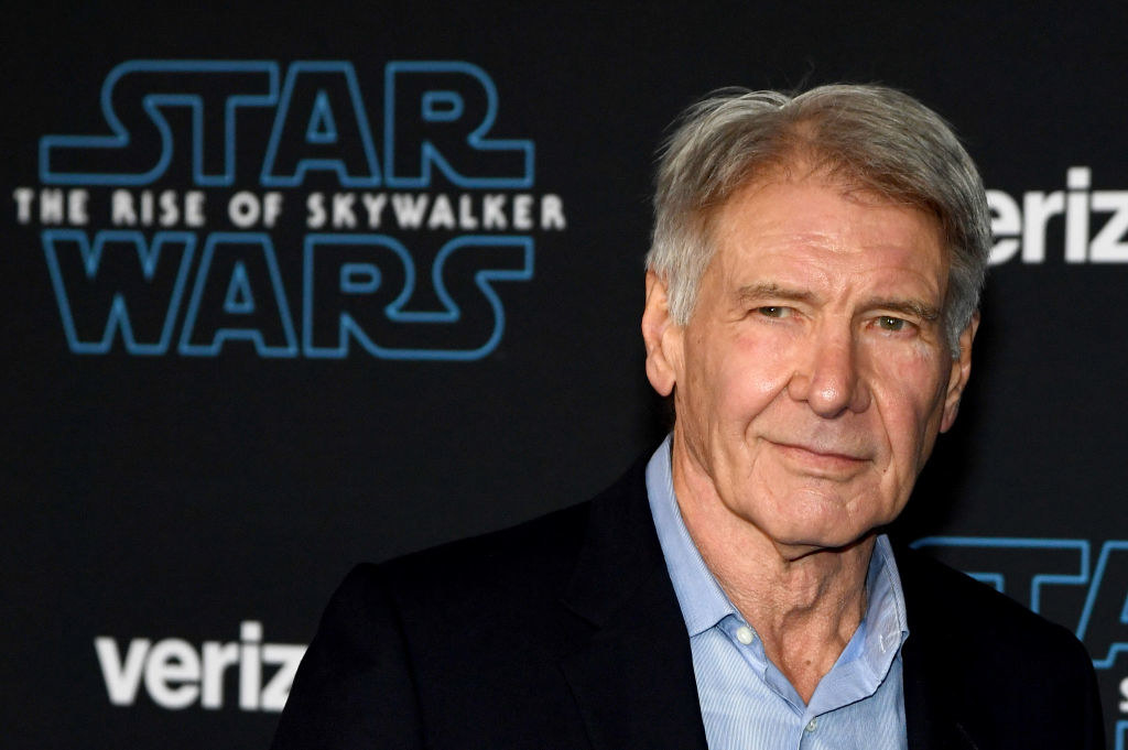 harrison ford smiling in front of a star wars the rise of skywalker poster on the red carpet