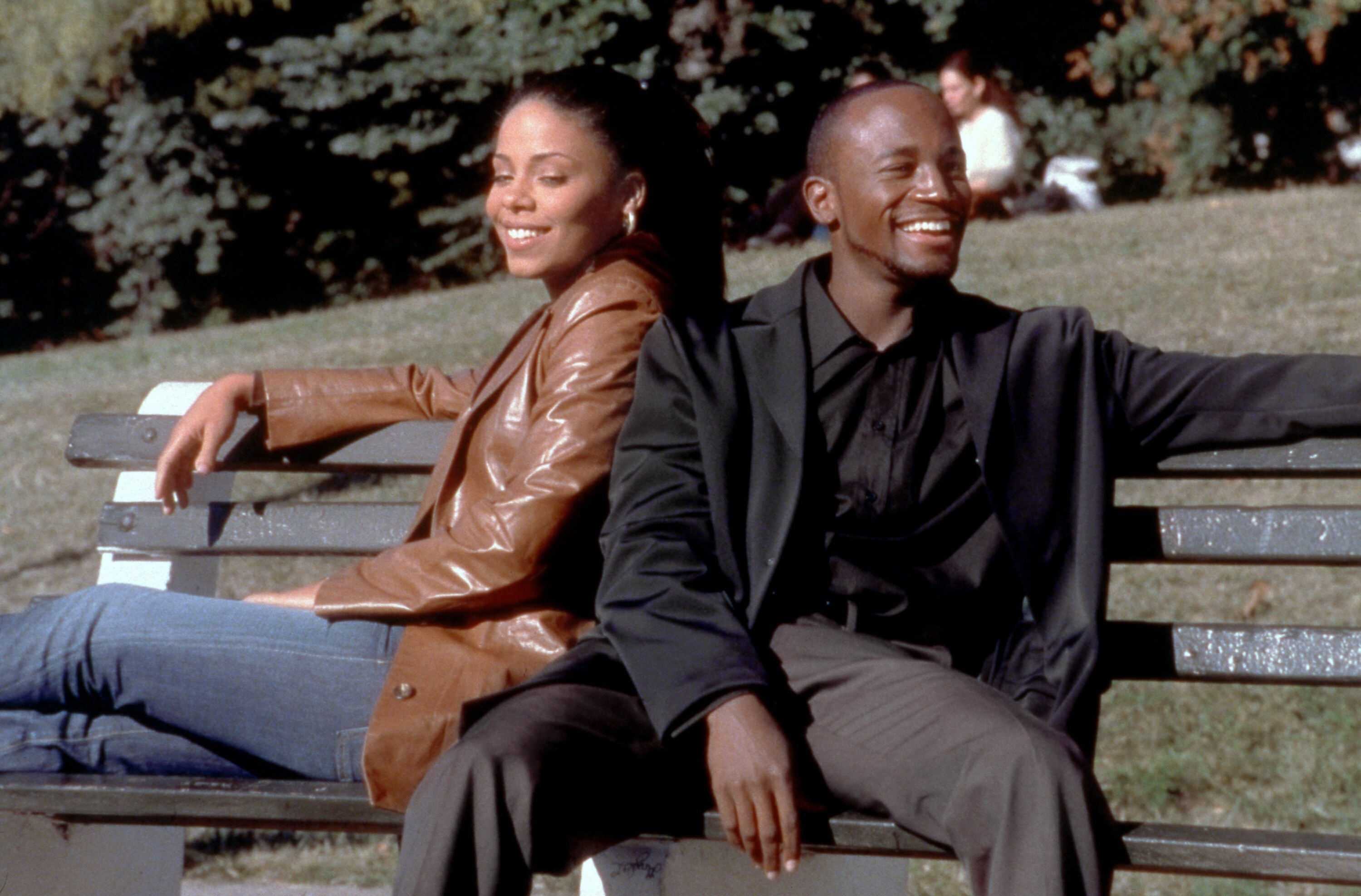 Black man and Black woman sit on a park bench smiling