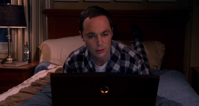 Sheldon lies on his bed in pyjamas looking at a laptop