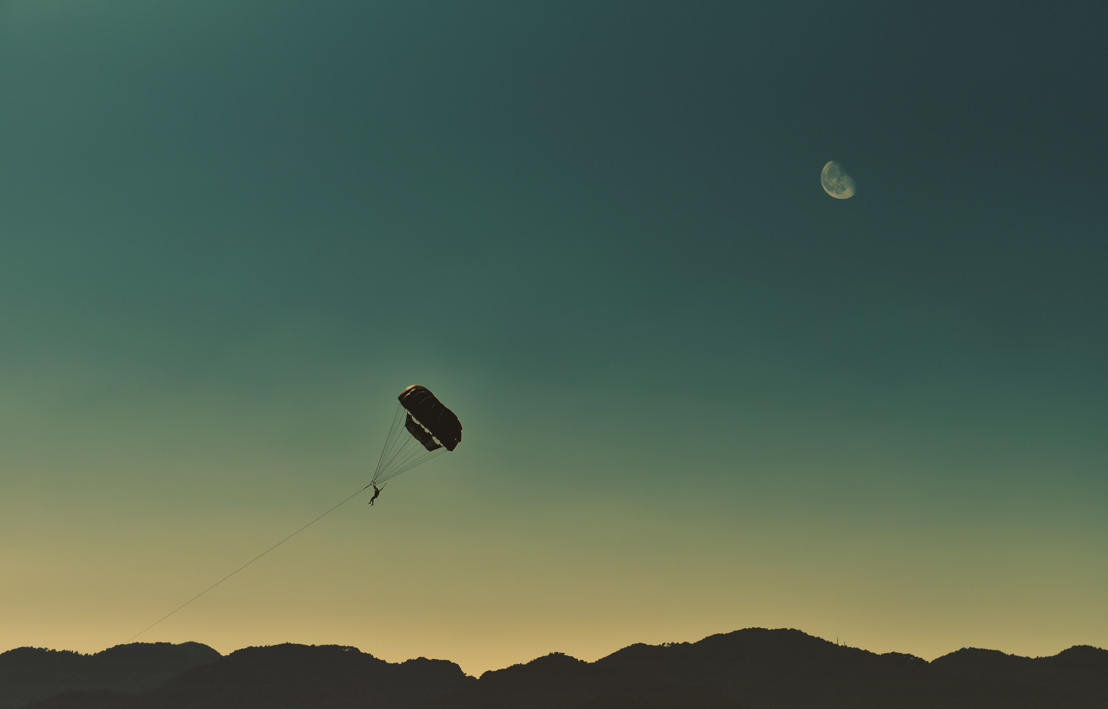 Parasailing in dusk against mountainous background and moon in the sky
