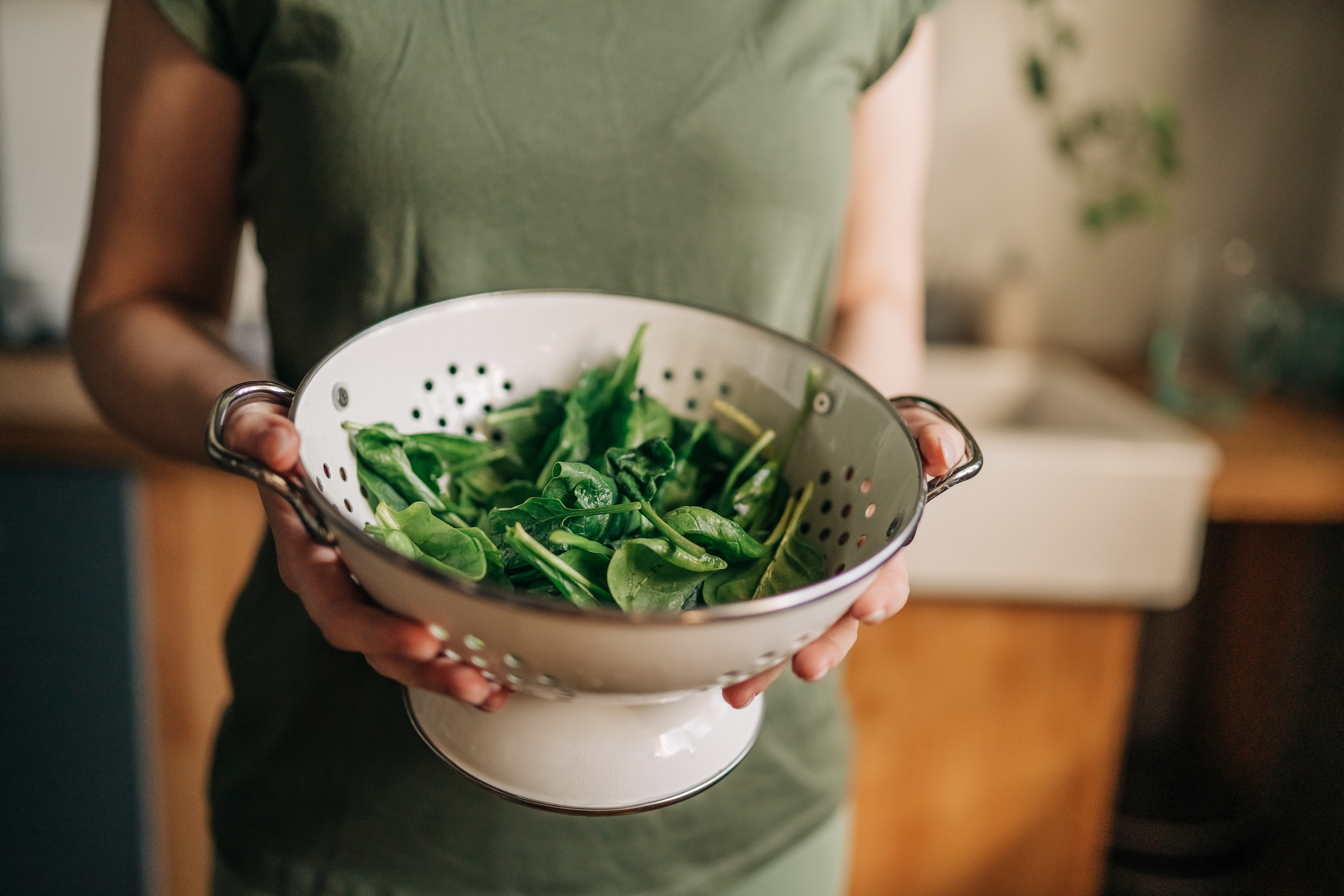 woman holds strainer of spinach