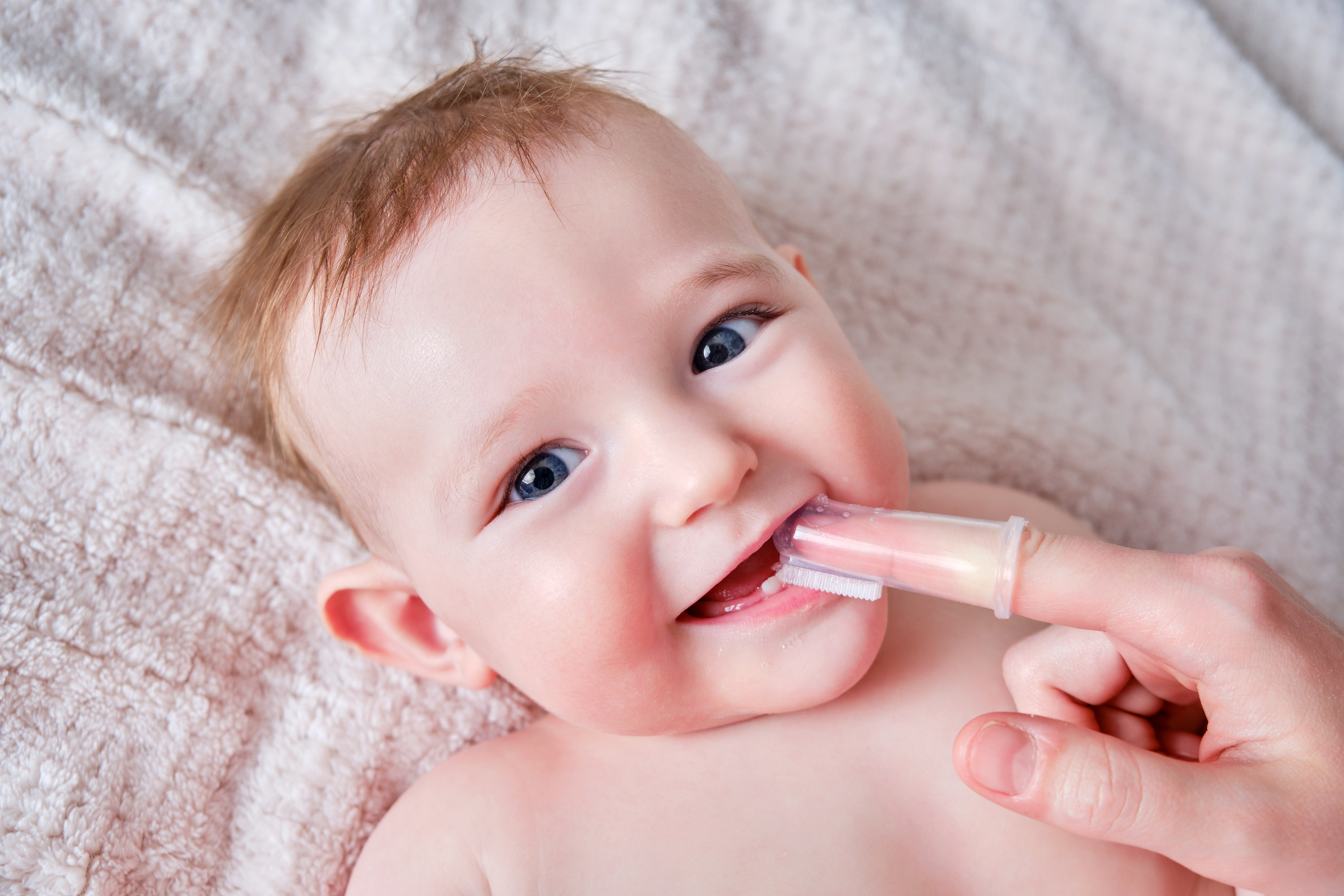 Mother hands brushing teeth with a finger brush of a happy infant baby
