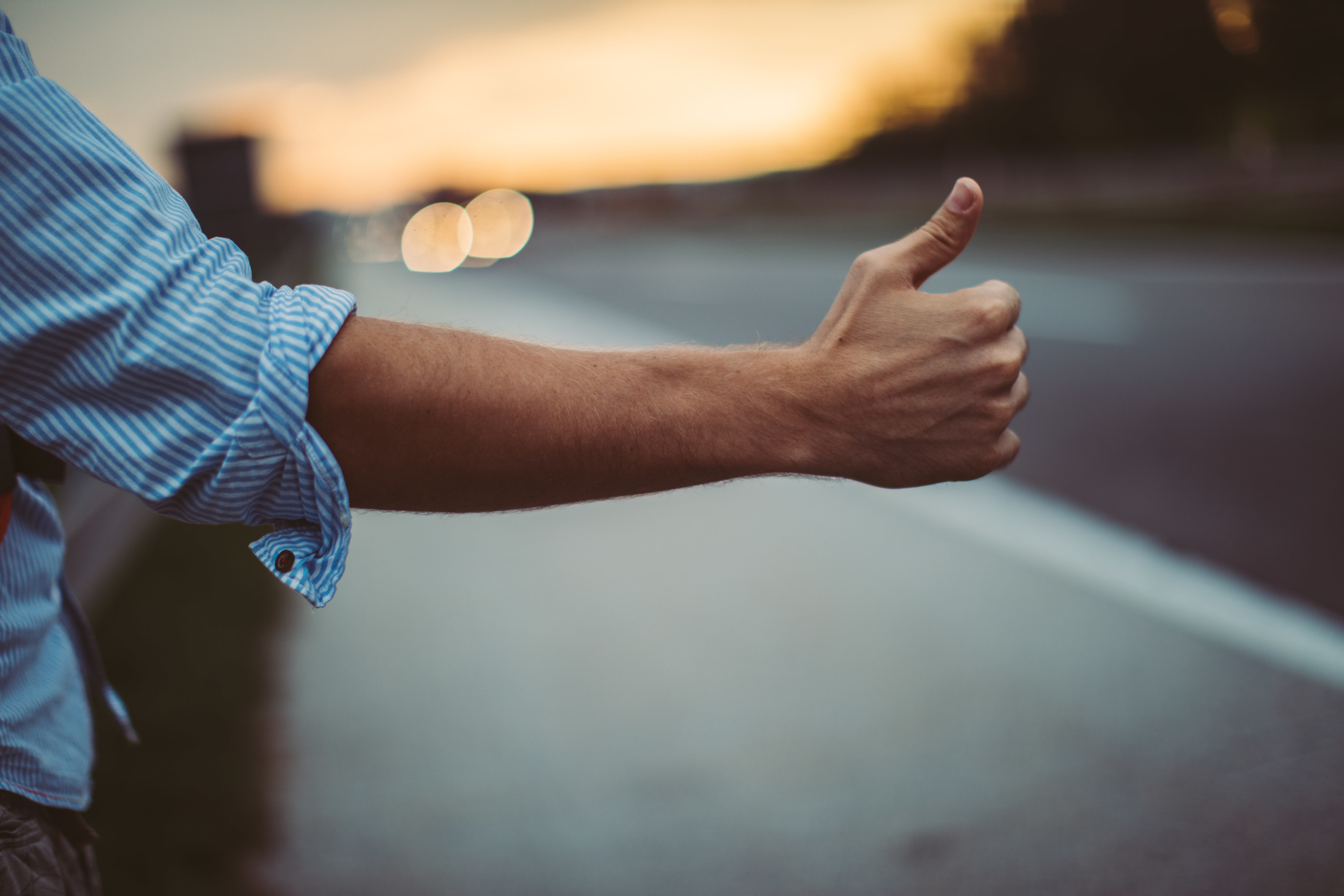man holding his thumb out on side of the road to hitchhike