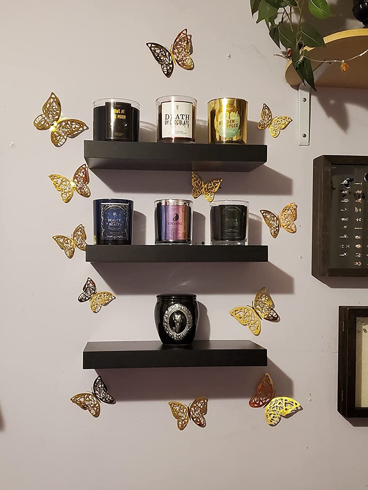 Black floating shelves holding candles, surrounding by gold butterfly wall decals