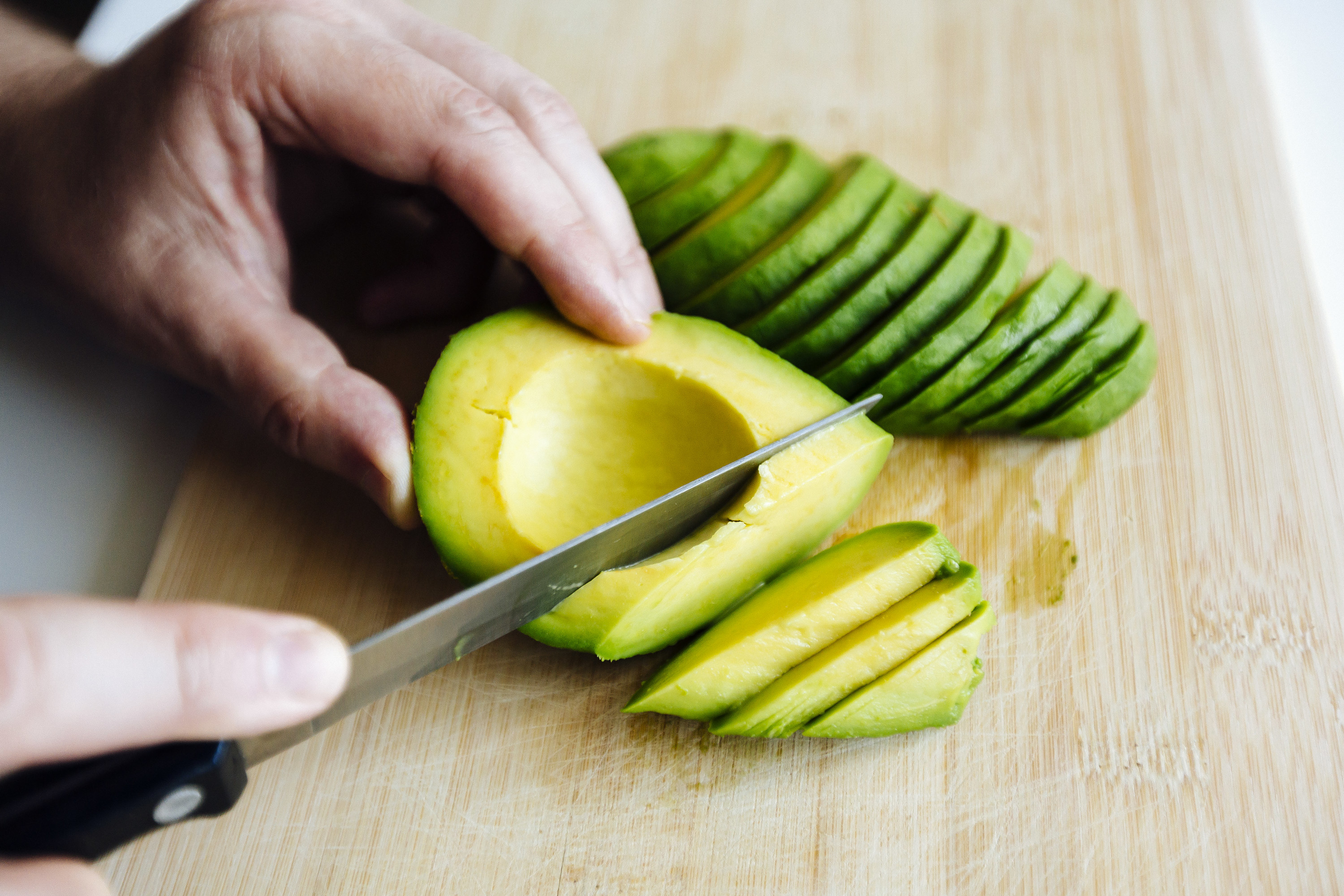 hands cutting avocado on a cutting board