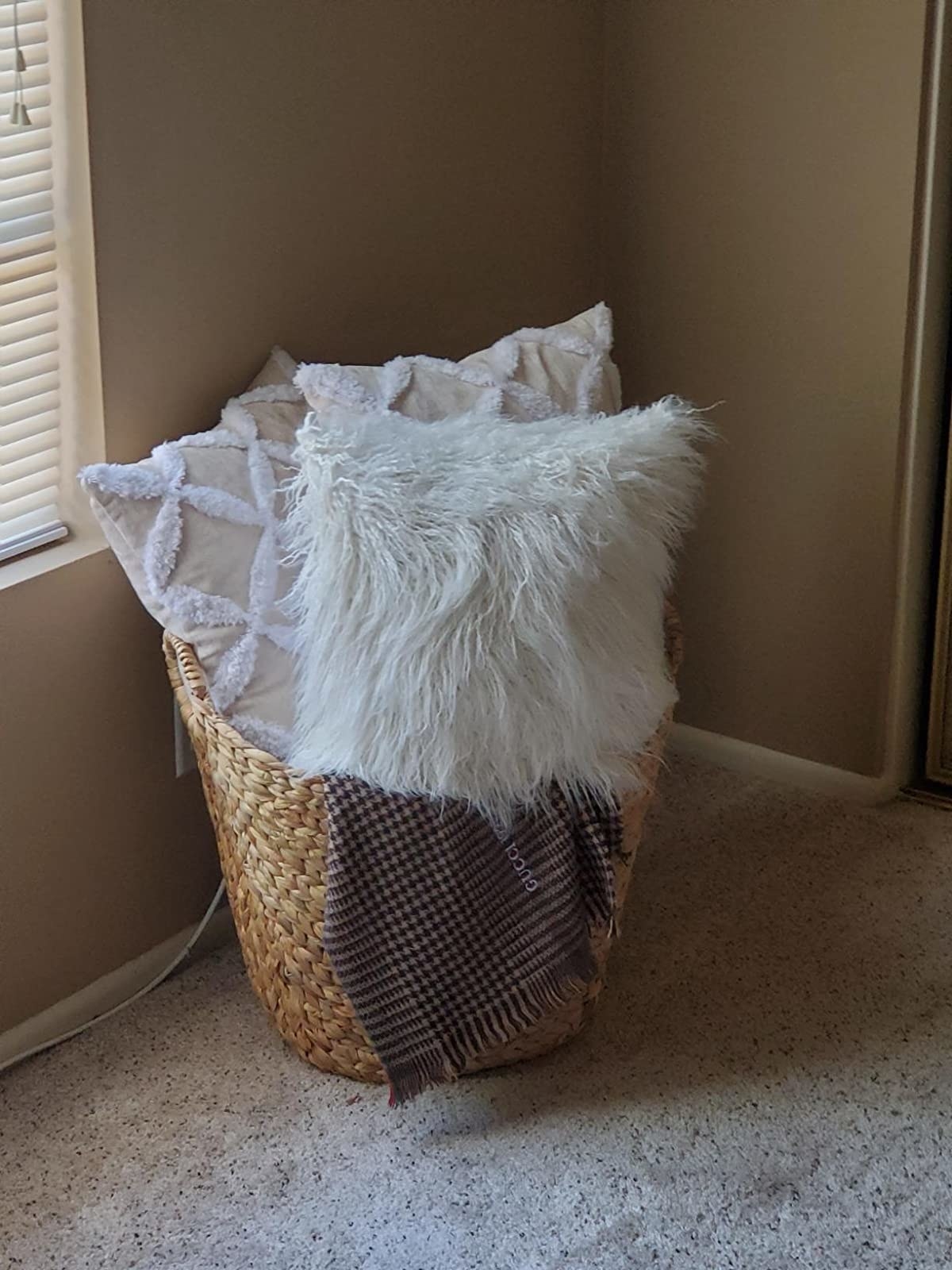 Woven floor basket holding white throw pillows and brown throw blanket