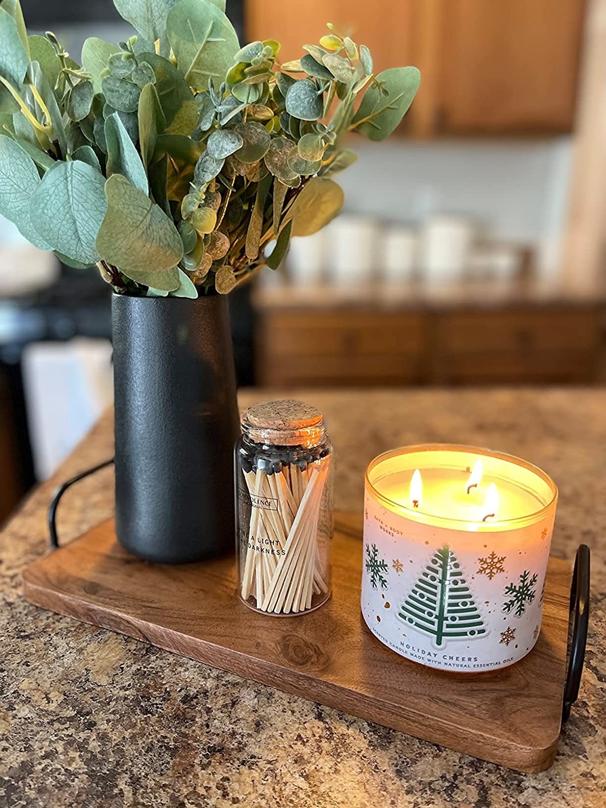 Black vase with eucalyptus leaves on wooden slab next candle and bottle of matches