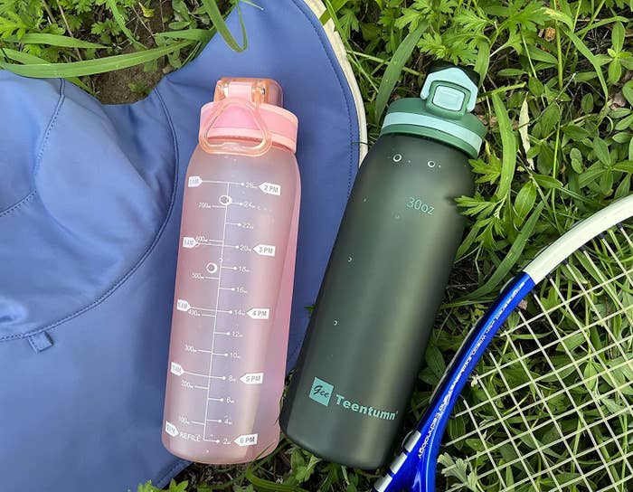 Two water bottles laid out on grass with tennis equipment