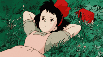 A girl with a red bow and a pink apron lays in a field of grass.
