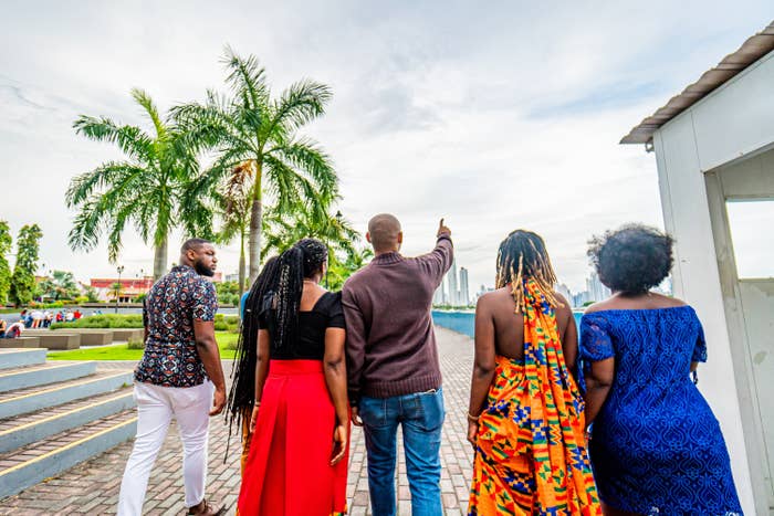 Local Tour Guide Pointing Forward While Walking with a Group of Cheerful, Fashionable Afro-Descendant Black Young Men and Women Together with a View of Panama City, Panama