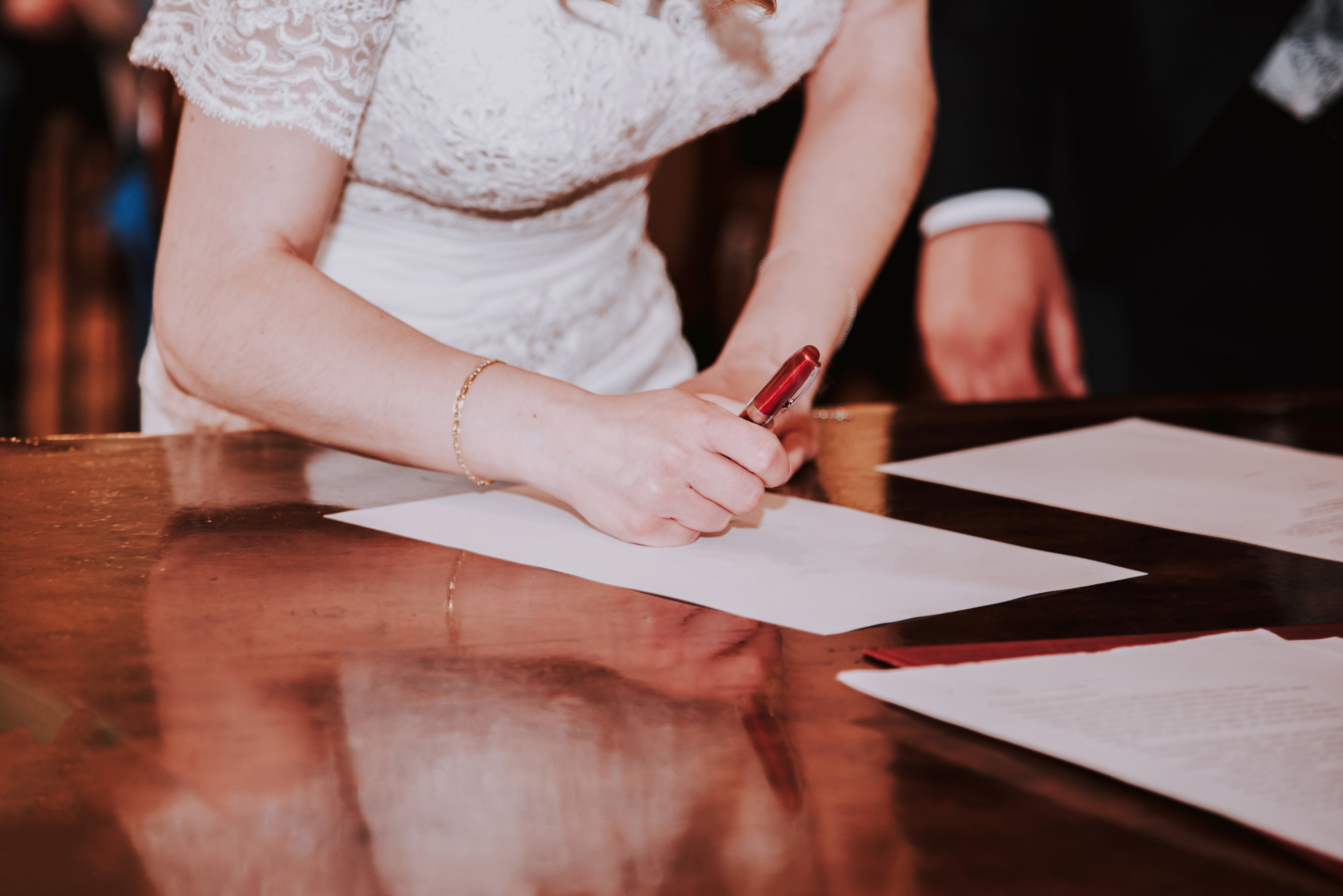A bride signs wedding papers alongside a groom