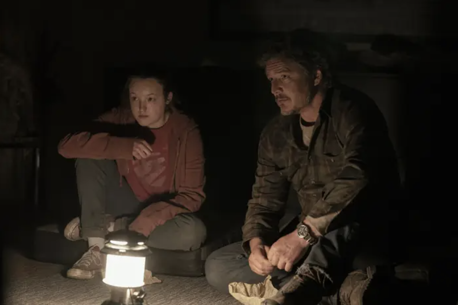 Actors Pedro Pascal and Bella Ramsey sit on the floor by a single lantern