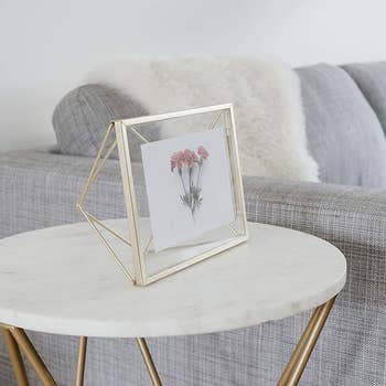 side view of brass photo frame with a wire design on the back, adding dimension sitting on a side table near a couch