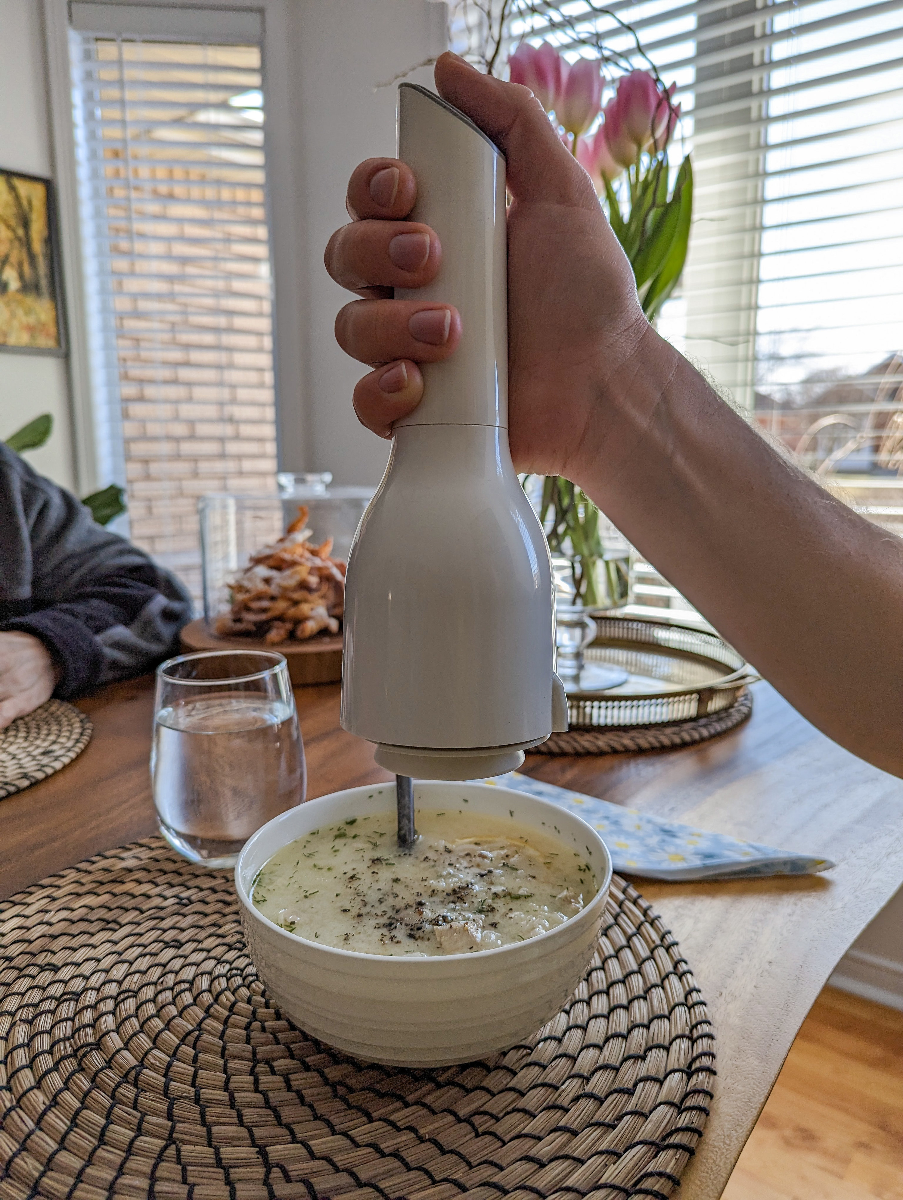 a person holding up the electric pepper mill over a bowl of soup