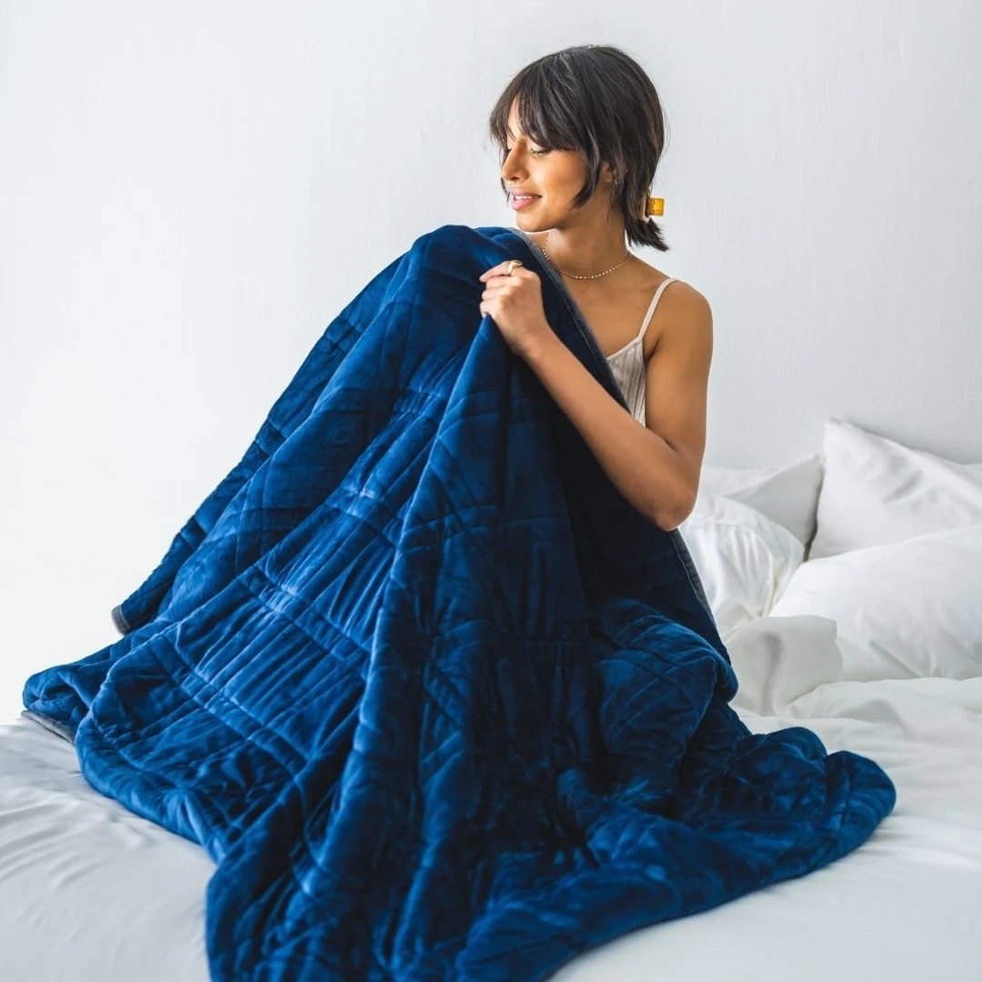 a model on a bed snuggled up with the blue weighted blanket