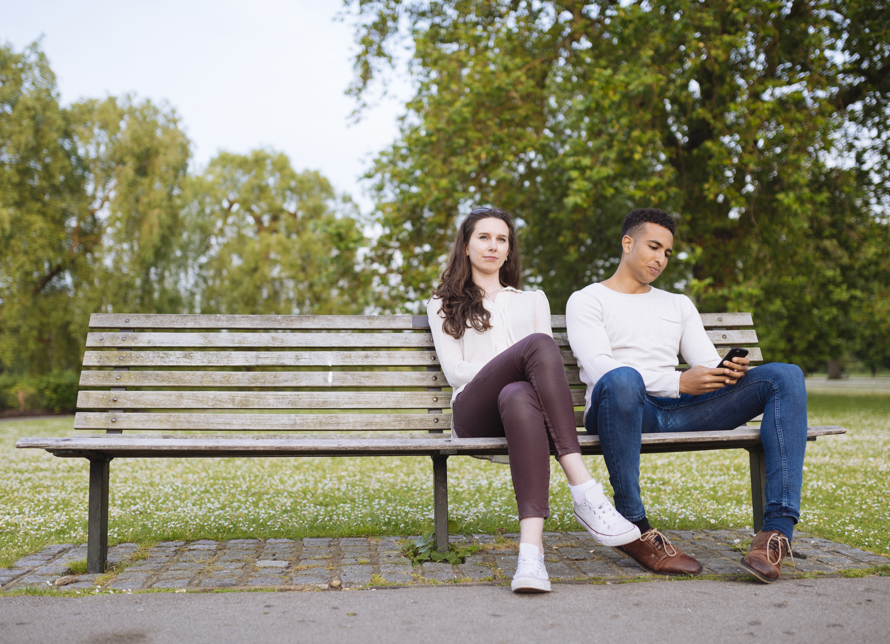 a man on his phone while the woman looking away on bench