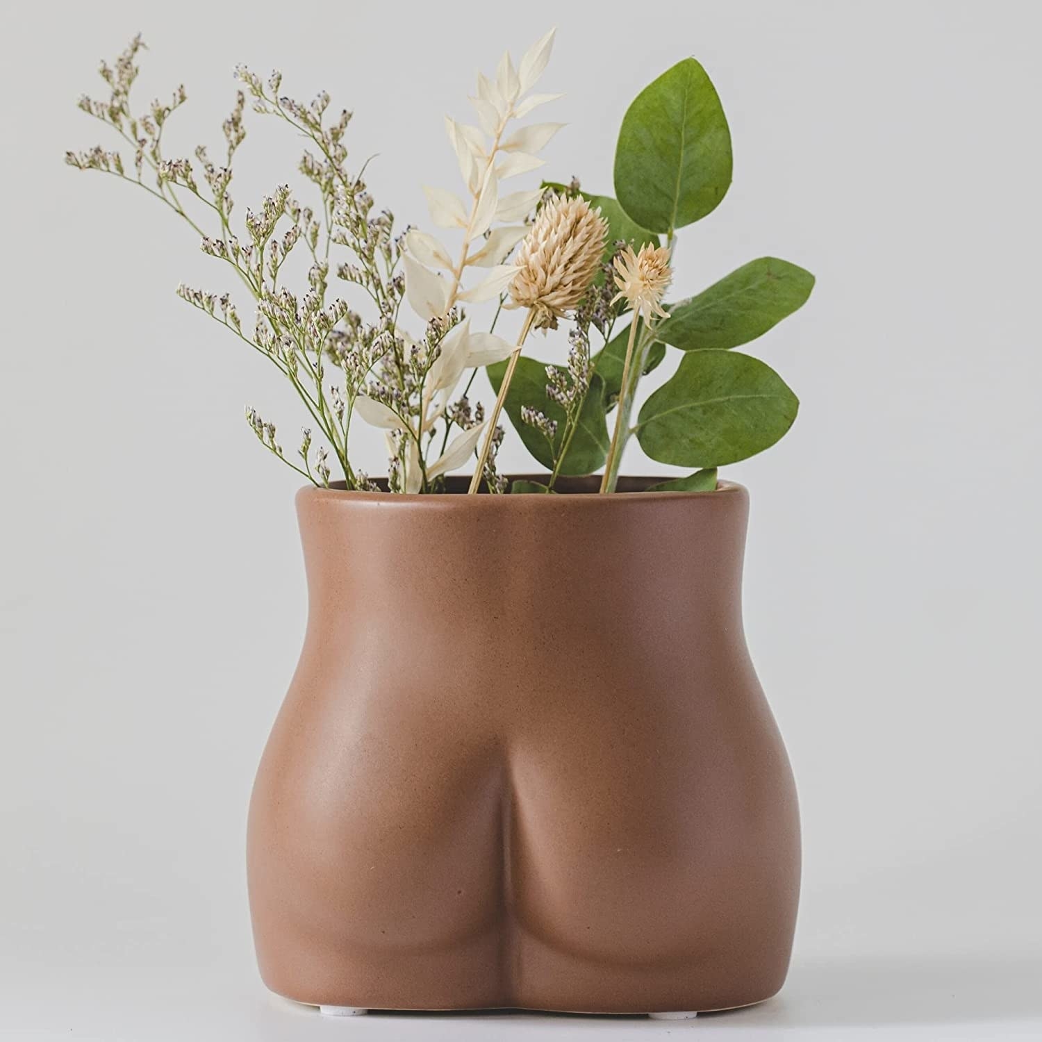 a butt-shaped planter filled with leafy sprigs