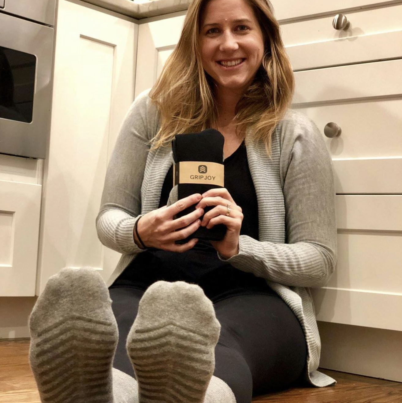 founder of the socks wearing them and holding a pack sitting on their kitchen floor