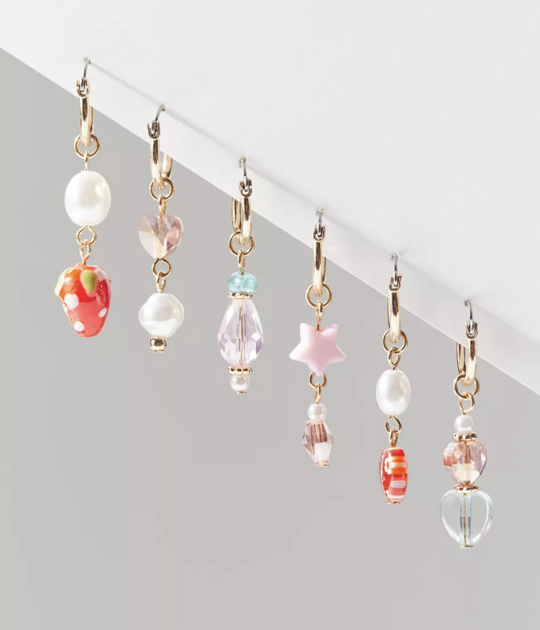 all six of the earrings hanging from a ledge in front of a plain backdrop