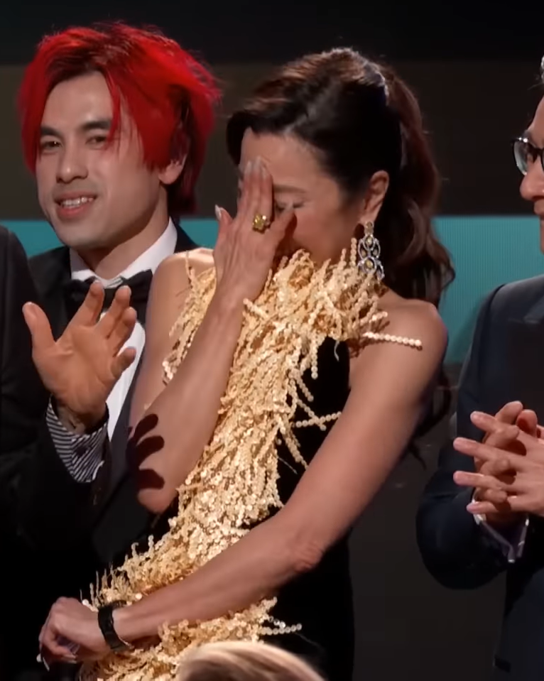 Michelle Yeoh puts her hand over her face in embarrassment while she laughs