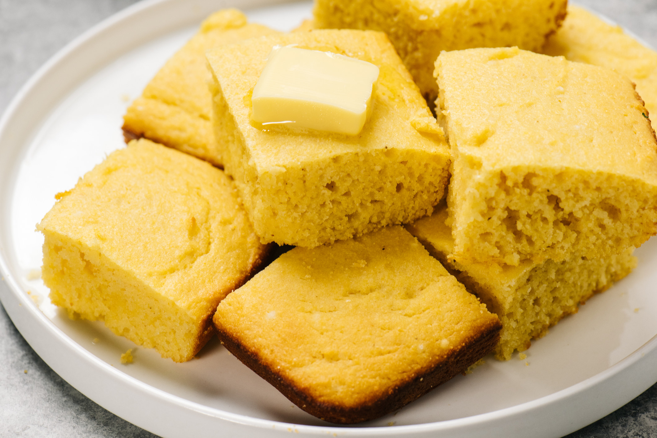 Plate of golden cornbread squares with butter.