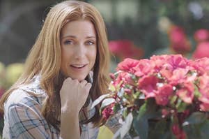 Kristen Wiig resting her chin on her hand as she stands near some blooming flowers in an SNL sketch