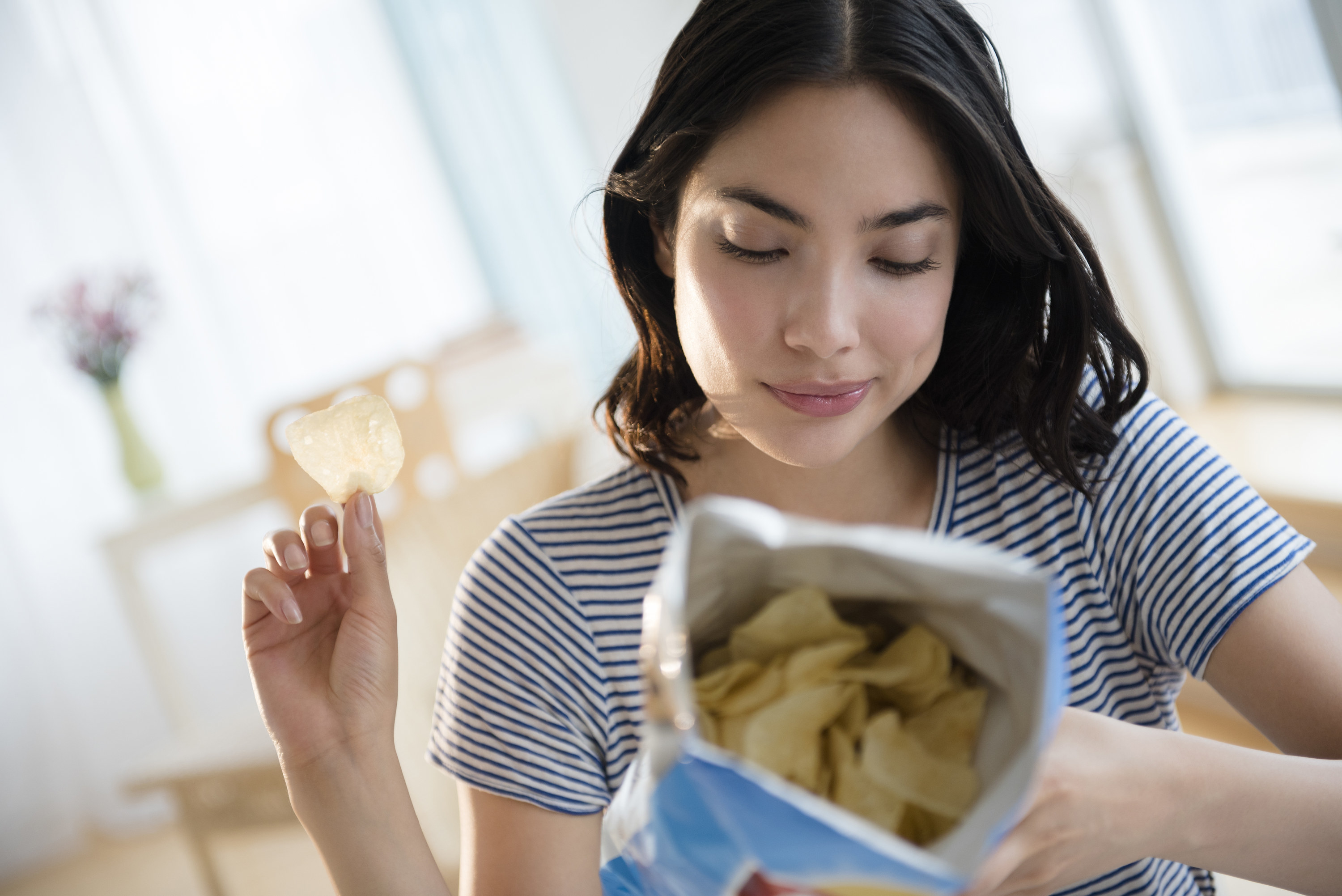 Woman looking at the back of an open potato chip bag with a single chip in her hand