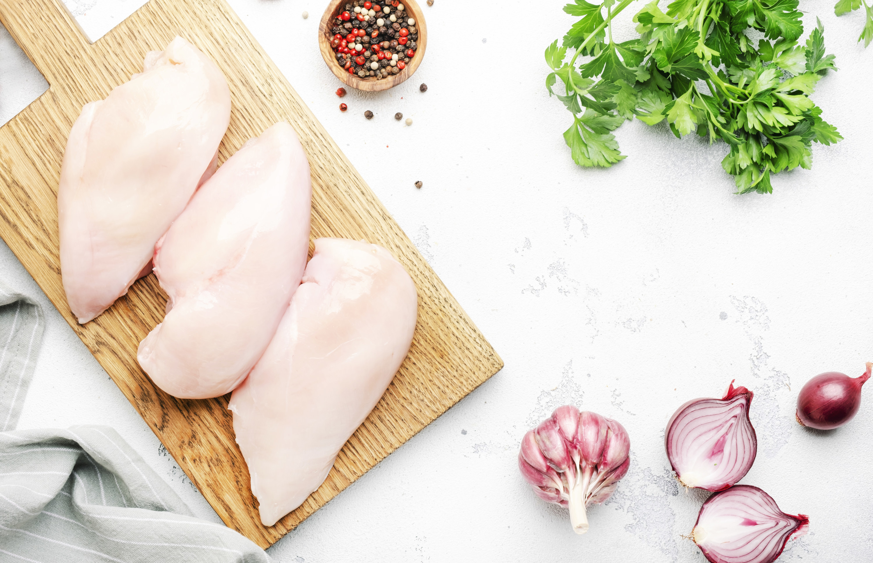Raw chicken breast fillet, meat on cutting board prepared for cooking with garlic, thyme, spices and pepper, top view