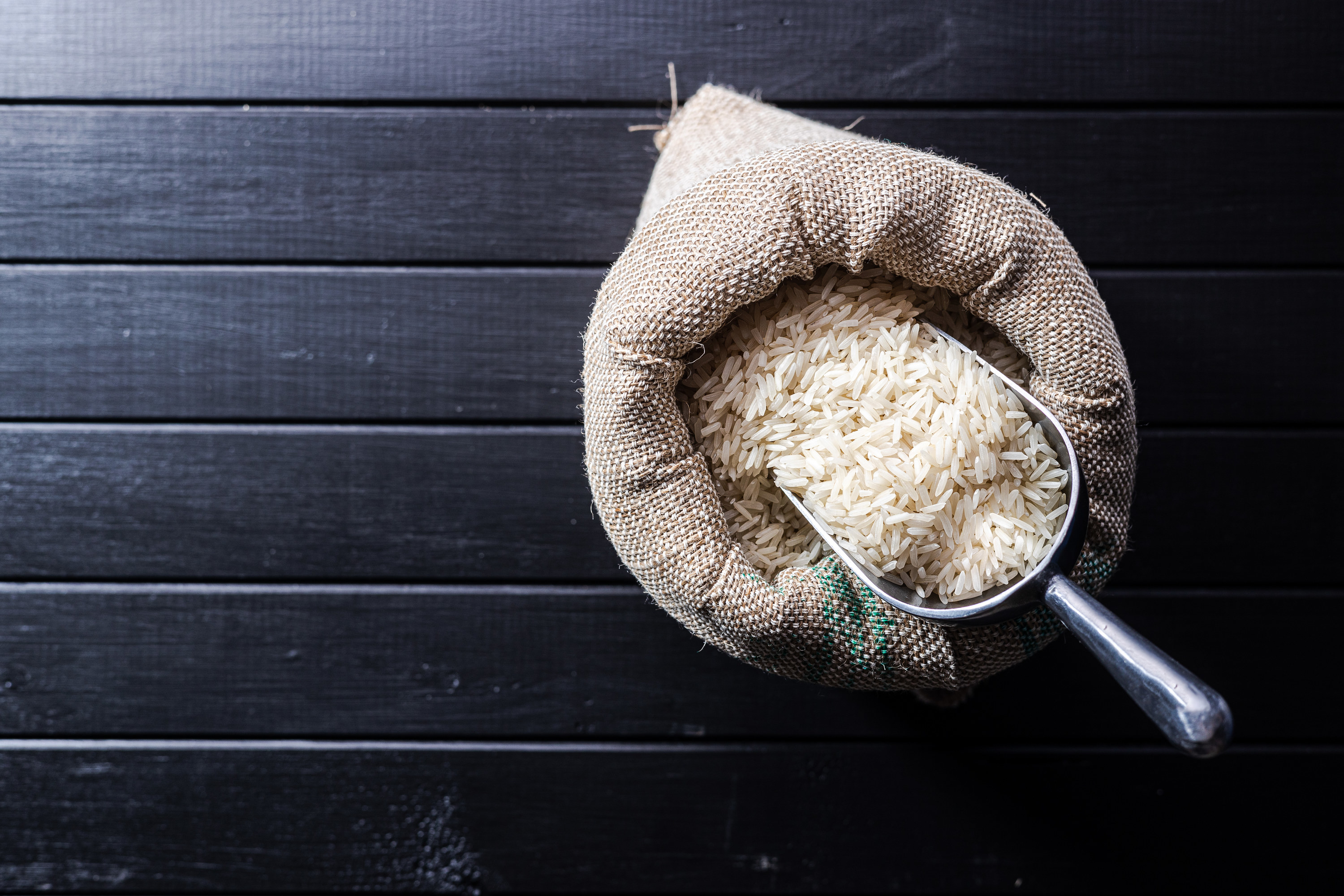 Uncooked white rice in a burlap sack on black table