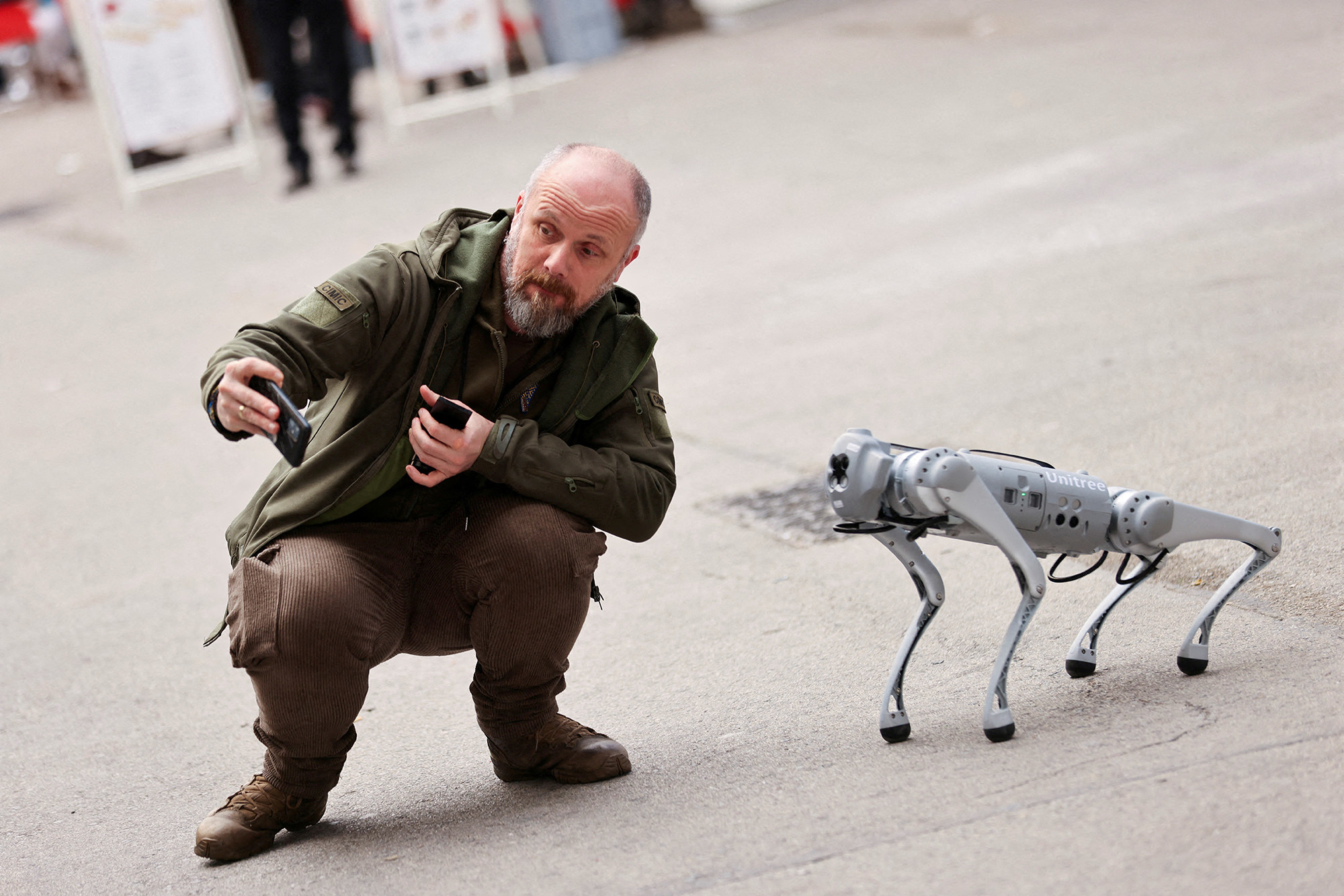 a bearded man crouches to take a selfie with a robot dog