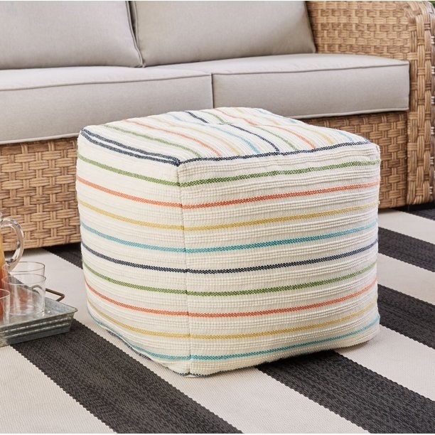 square white pouf with colorful stripes on an rug