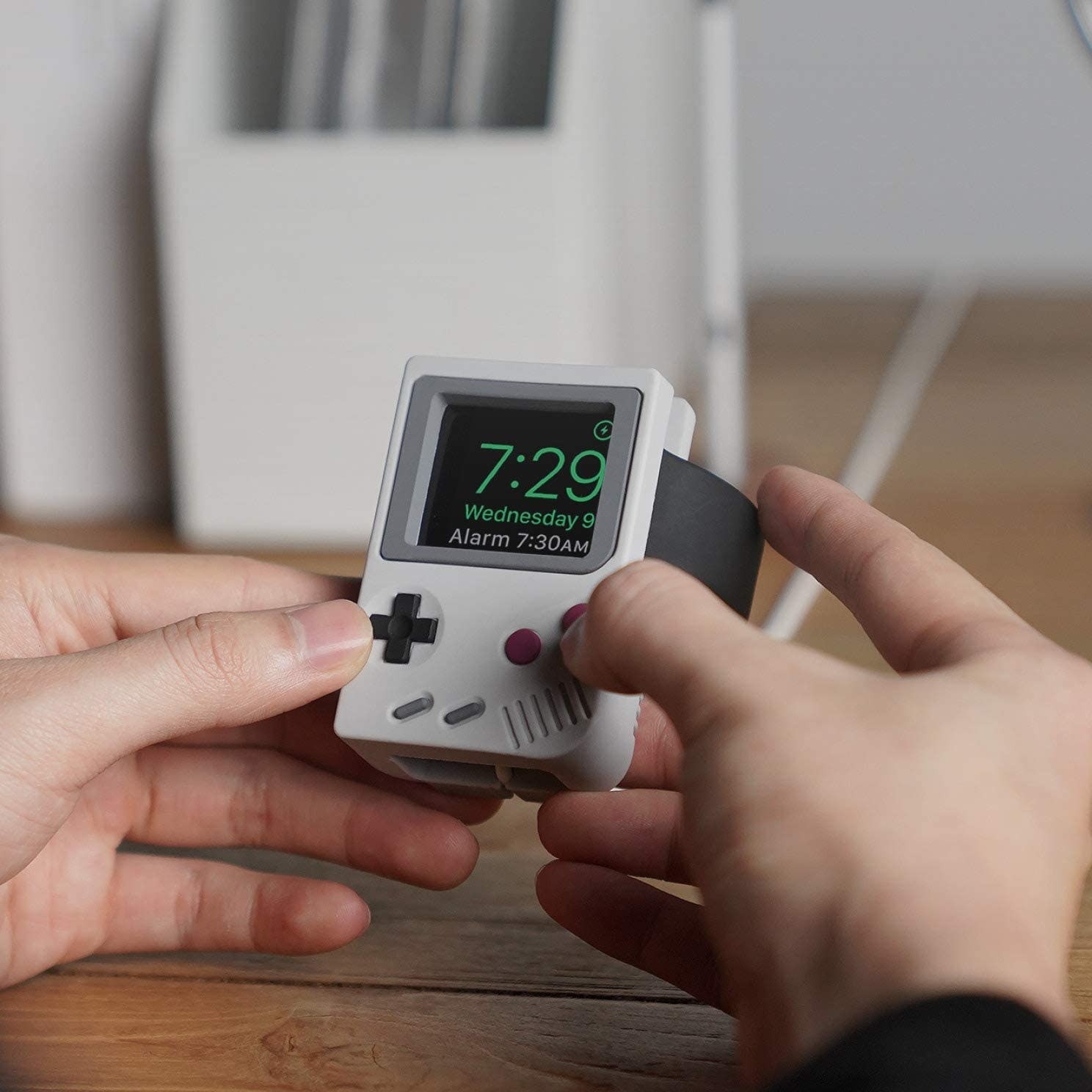 a person holding their apple watch while it sits in the nostalgic gameboy-shaped stand