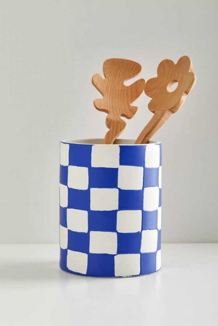 A blue and white checkered utensil holder with two salad spoons in it