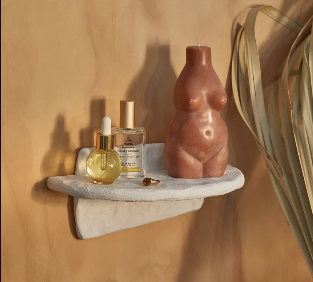 A white wall shelf with perfume and a vase on it