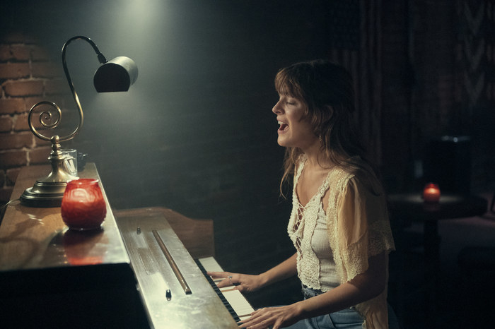 Riley plays the piano in a dark room on the show