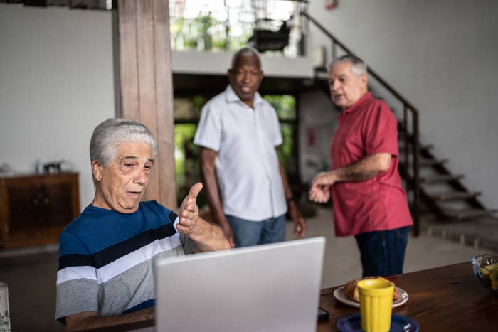 Man gesturing at a laptop as two men stand behind him