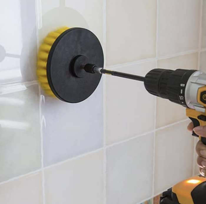 a person using the brush attachment on their drill to clean a tile backsplash
