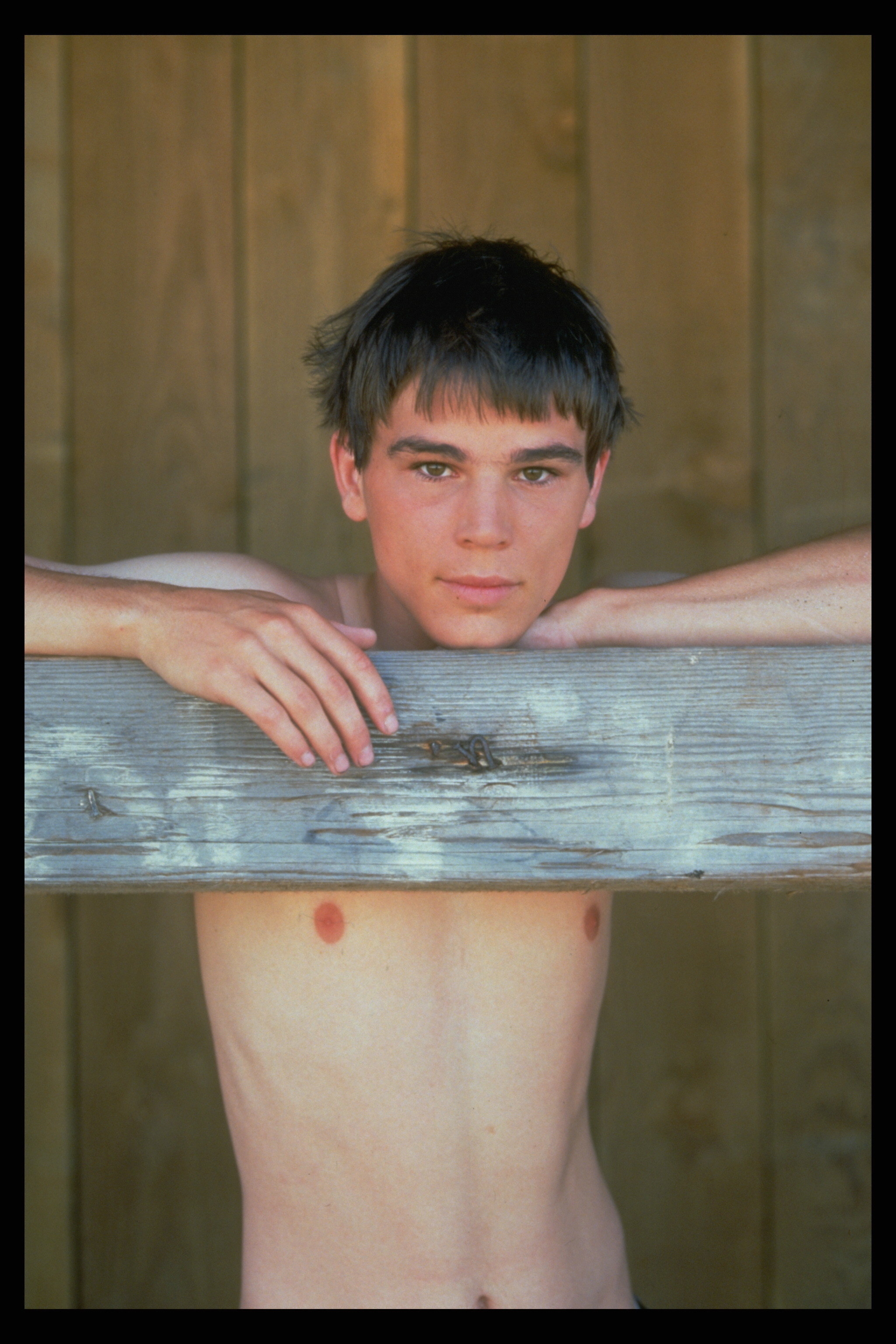 closeup of a shirtless Josh with his arms on a wooden fence