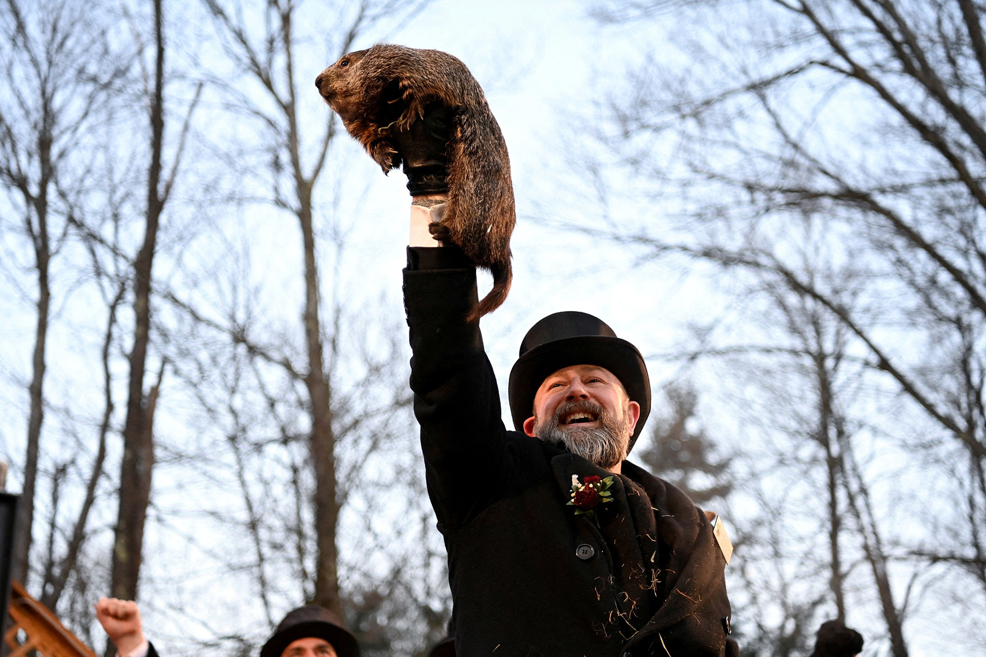 a man in a top hat holds up a groundhog named phil outside in pennsylvania