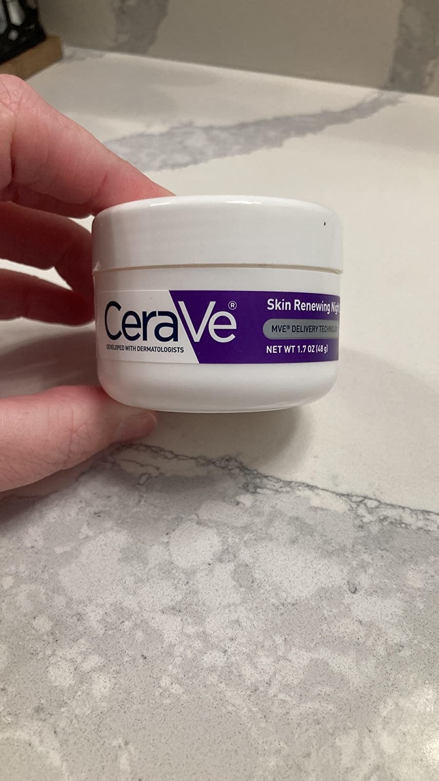 reviewer  holding the white and purple tub of moisturizer