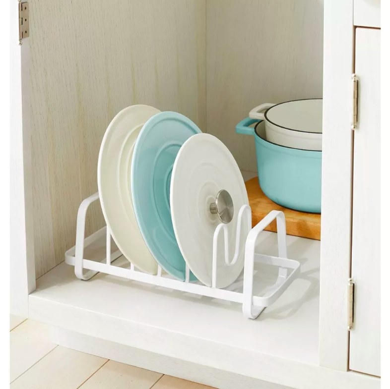 Cooking pot lids in a white wire organizer inside a kitchen cabinet