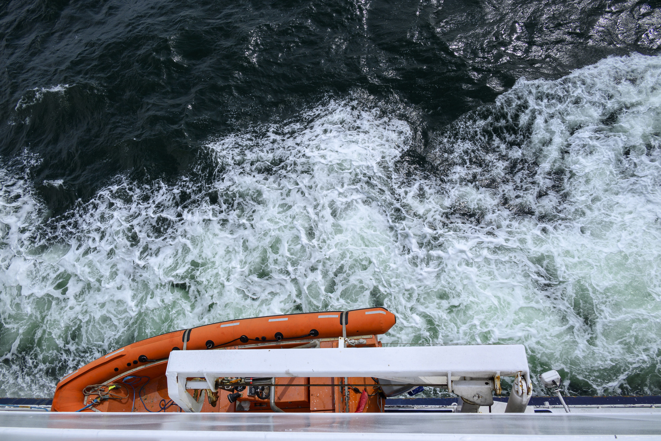 Churning sea seen from a ship, with a lifeboat above the water