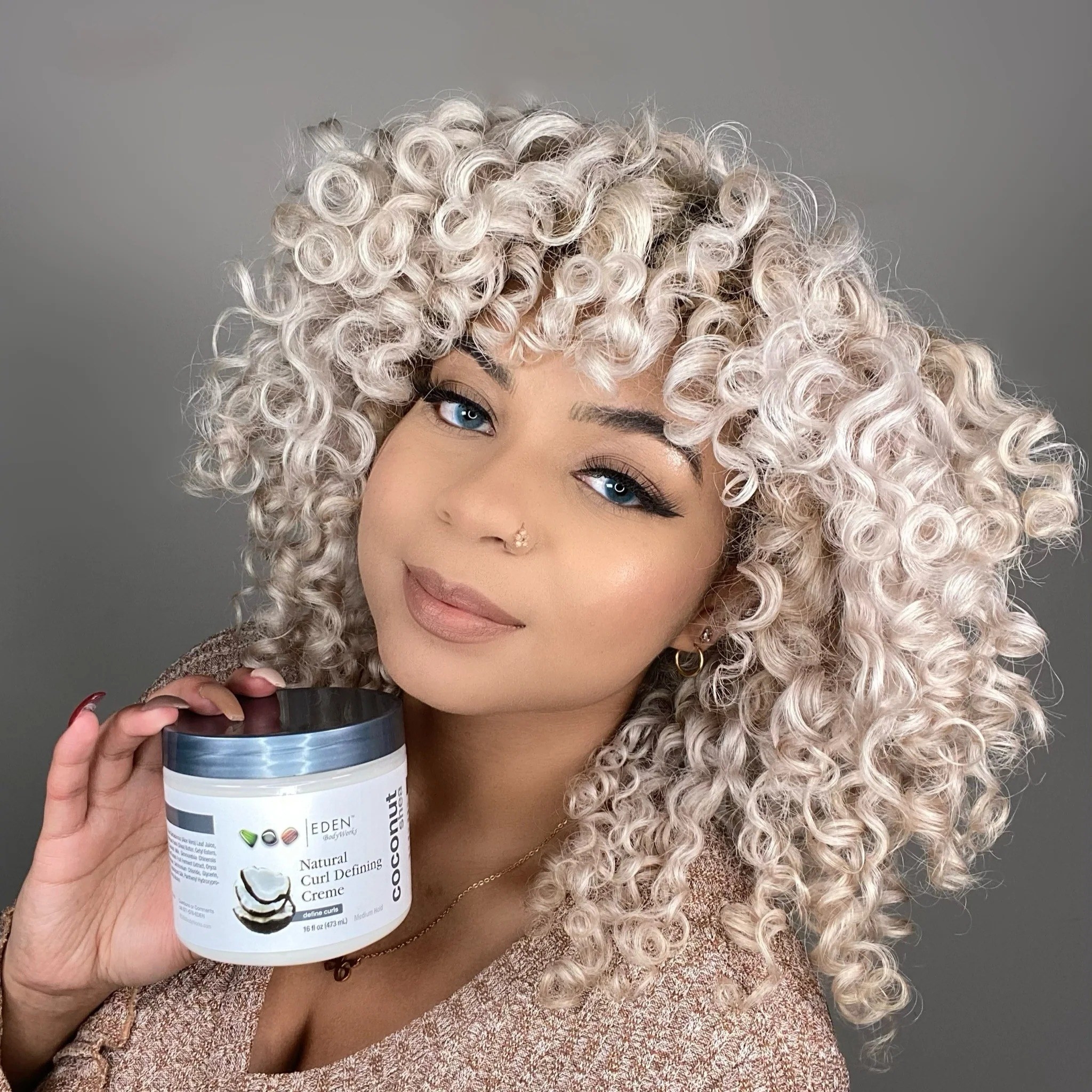 a model with soft-looking defined curls holding the jar of hair creme