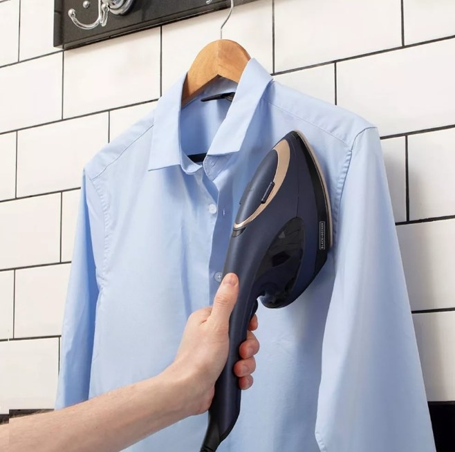2 in 1 steamer iron steaming a blue shirt that is hung in a bathroom
