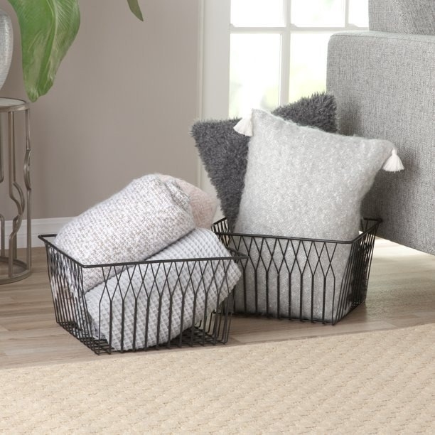Black iron wire baskets on the floor filled with pillows and blankets