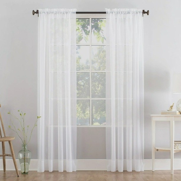 A white curtain panel on a curtain rod in a room near a window