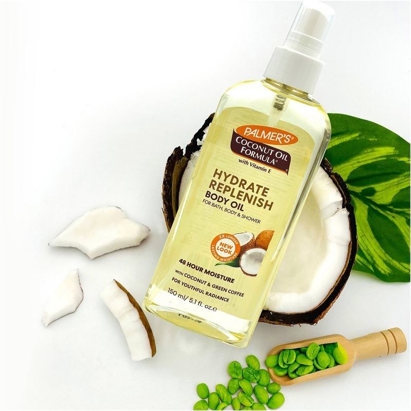 A bottle of body oil with a sliced coconut and plant seeds