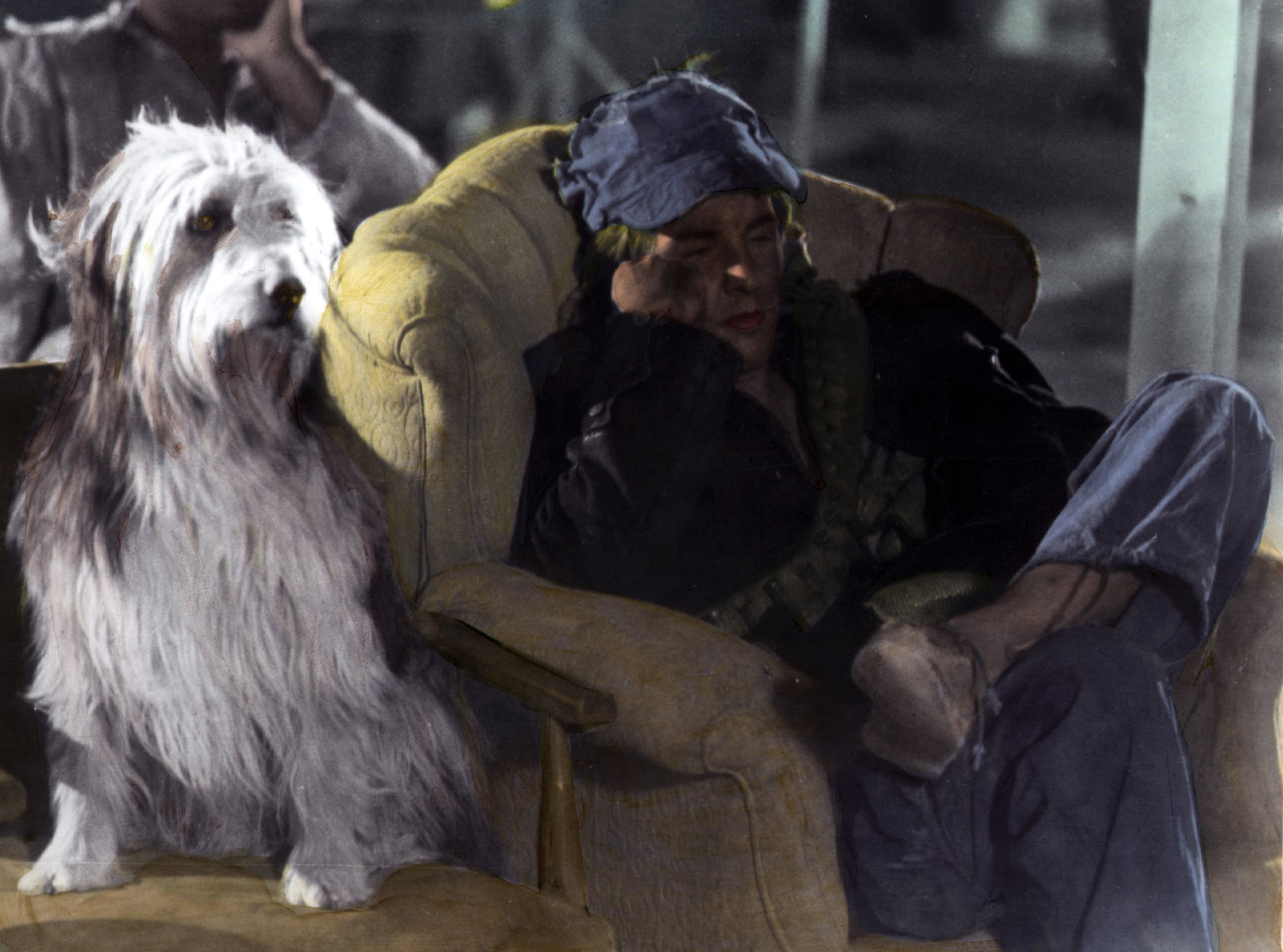 A young man in a filthy chair stares in the distance next to his shaggy dog