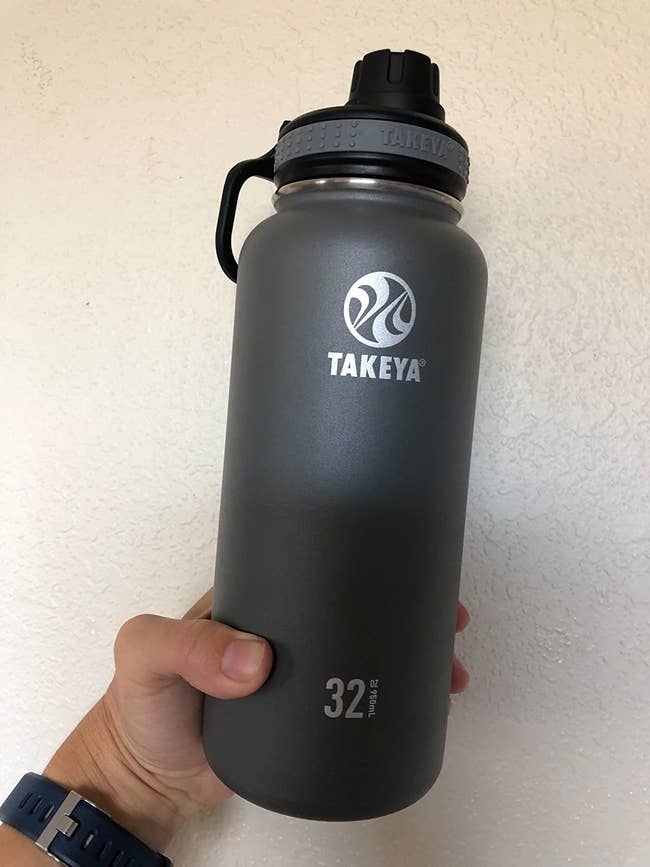 A reviewer holding a black 32 ounce water bottle