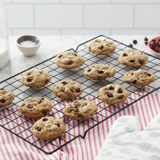 twelve chocolate-chip cookies resting on a black cooling rack